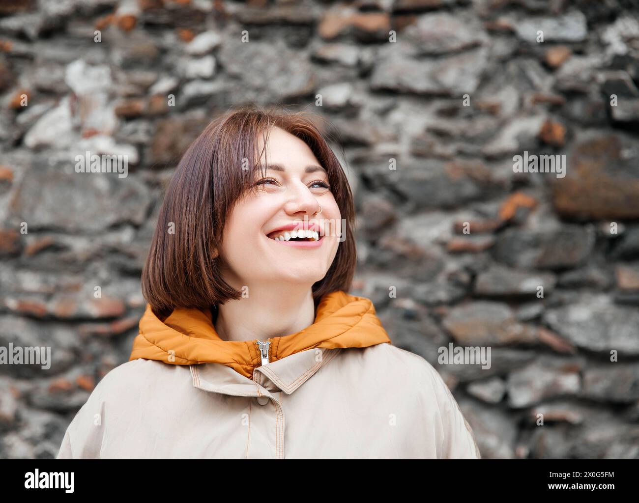 Fröhliche junge Frau lächelt mit Steinmauer Hintergrund Stockfoto