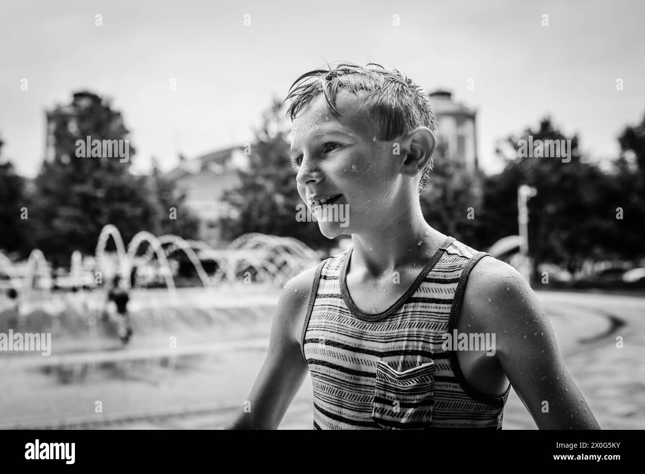 Kind im Sommer mit Wassertropfen am Stadtbrunnen bedeckt Stockfoto