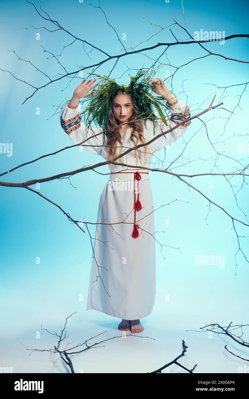 Eine junge Magka in kunstvoller traditioneller Kleidung steht anmutig vor einem mystischen Baum mit Ästen. Stockfoto