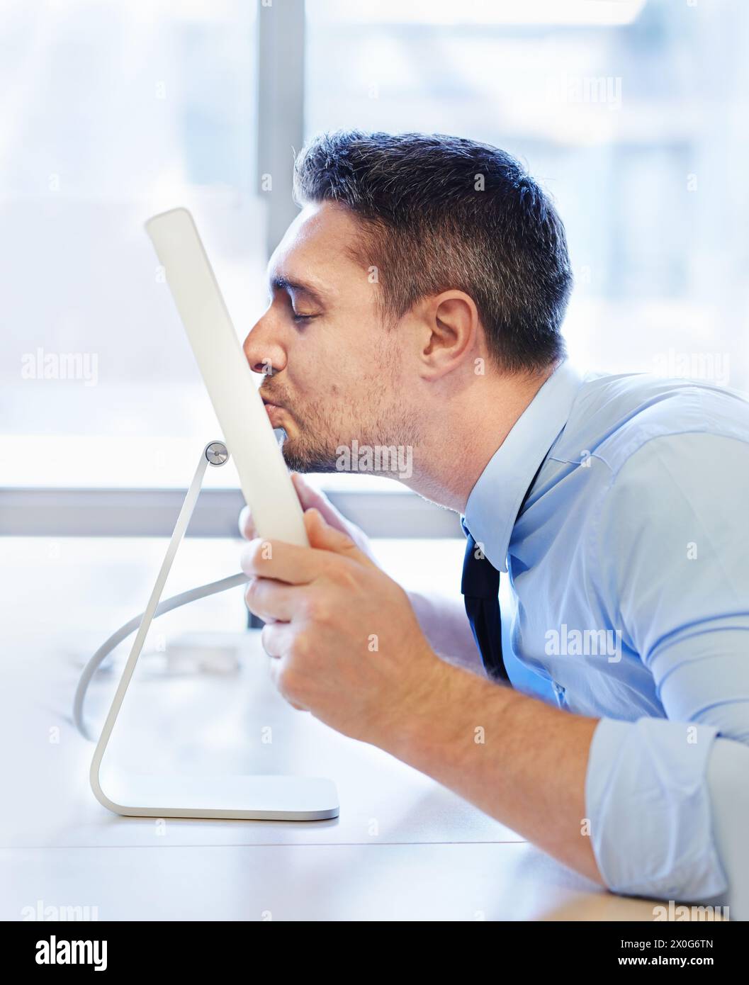 Glücklicher Geschäftsmann, küssender Bildschirm und Büro für Beruf in der Karriere, Liebe für Organisationsprojekte oder Crush online. Editor, Technologie und virtuell Stockfoto