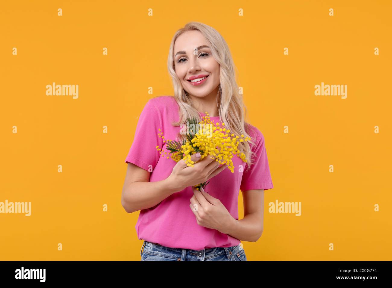 Glückliche junge Frau mit wunderschönem Blumenstrauß auf orangem Hintergrund Stockfoto