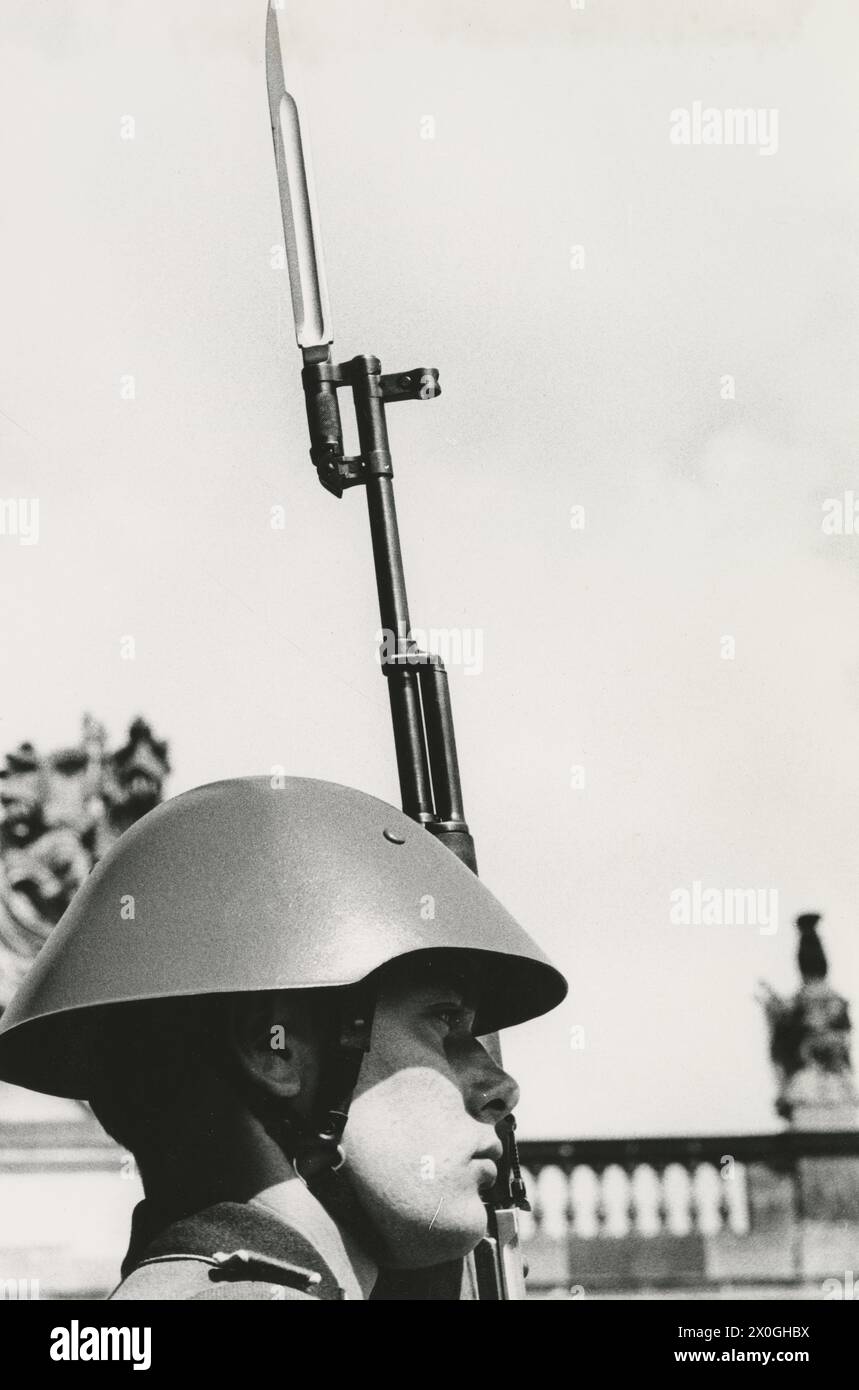 "Wachsoldat der Nationalen Volksarmee mit Gewehr und Bajonett und Stahlhelm vor der "Neuen Garde", unter den Linden, im Hintergrund die Dachfiguren des Waffenarztes. [Automatisierte Übersetzung]“ Stockfoto