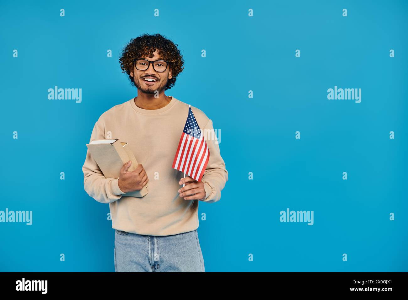 Ein Mann hält stolz ein Buch und eine amerikanische Flagge, die vor blauem Hintergrund in einem Studio steht. Stockfoto