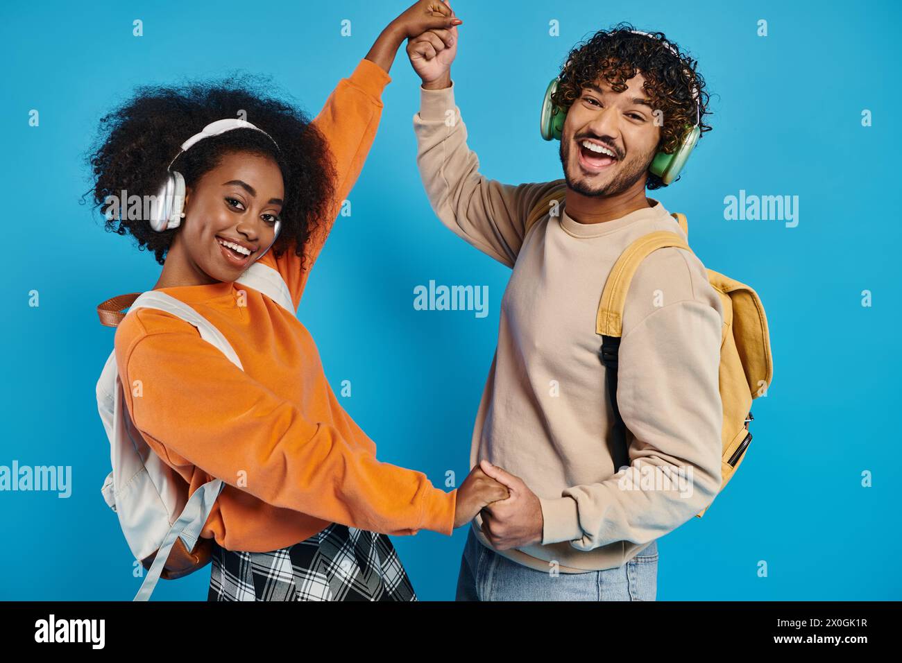 Ein Mann und eine Frau tanzen zusammen, tragen Kopfhörer und drücken Freude und Verbundenheit durch Bewegung vor blauem Hintergrund aus. Stockfoto
