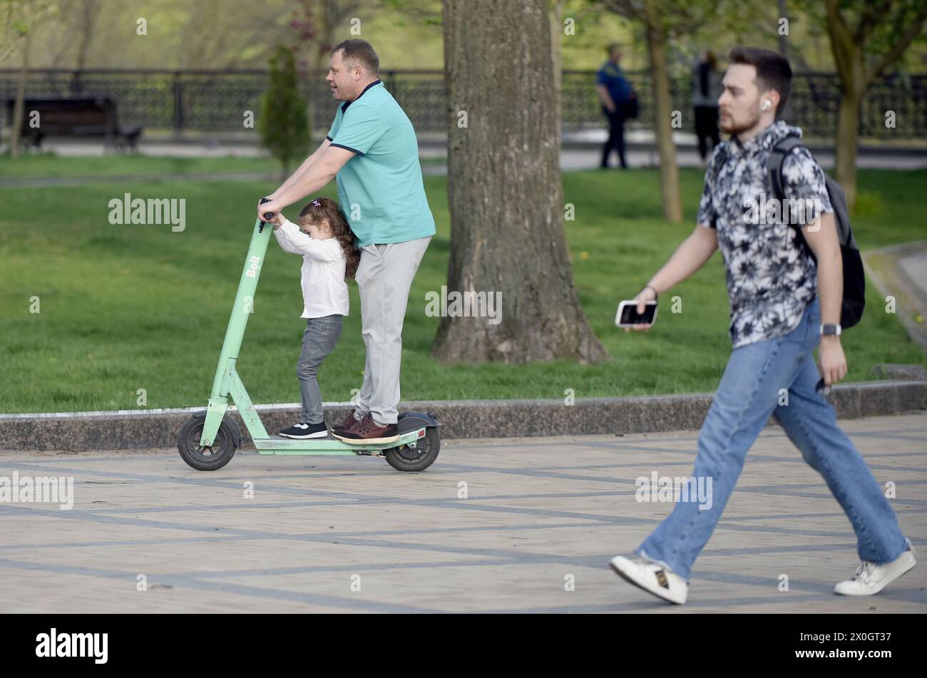 KIEW, UKRAINE - 11. APRIL 2024 - Ein Mann und ein Mädchen fahren mit einem Elektroroller im Wolodymyrska Hill Park in Kiew, Hauptstadt der Ukraine. Stockfoto