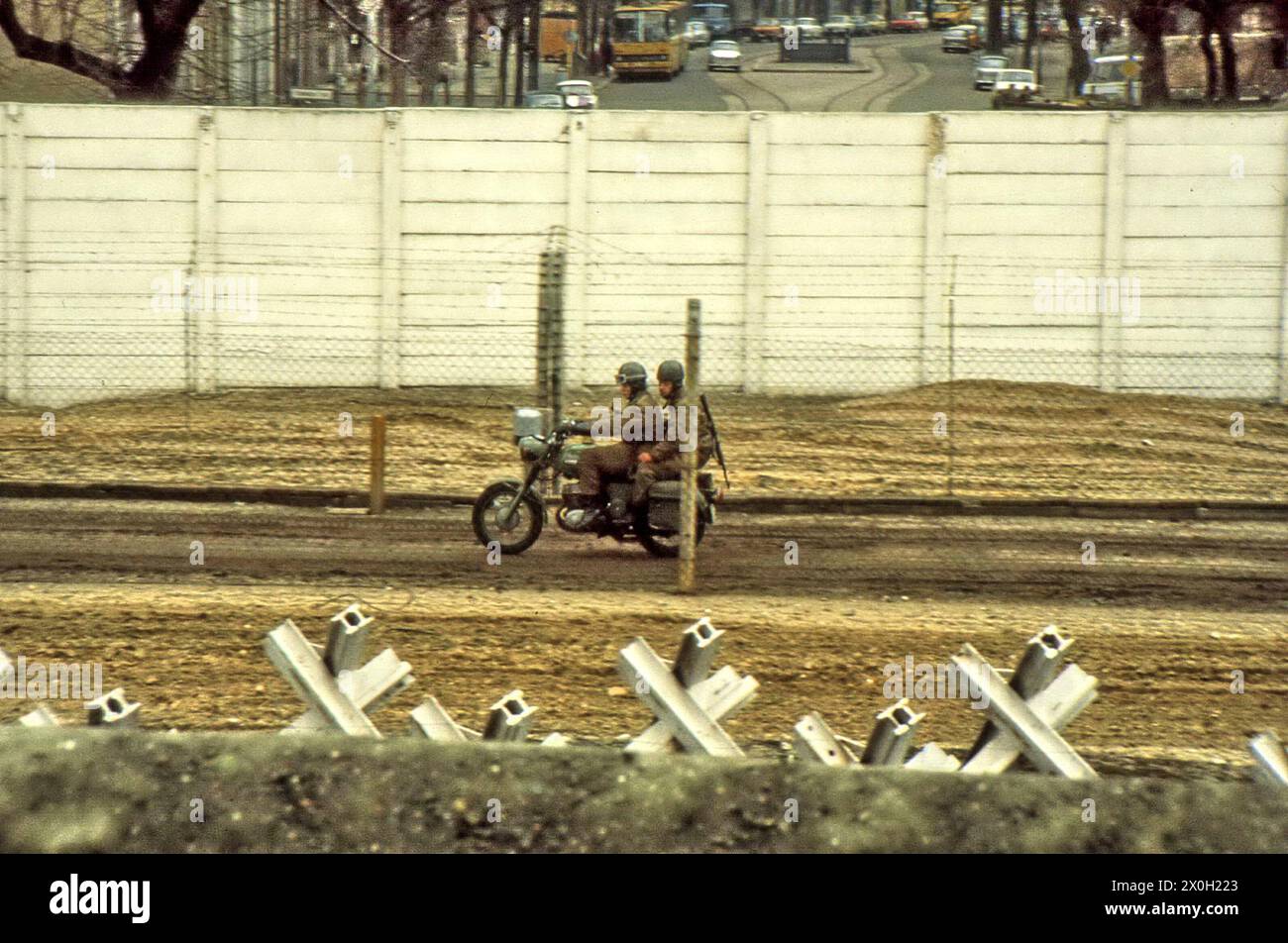 Soldaten der Nationalen Volksarmee (NVA) auf einer Motorradfahrt entlang der Grenze. Im Vordergrund befinden sich Panzerschranken und im Hintergrund eine Straße in Ost-Berlin. Stockfoto