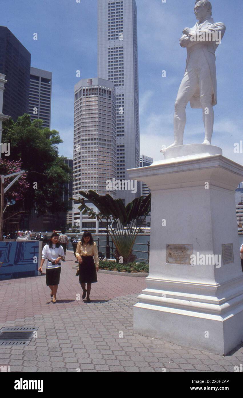 Die Statue von Sir Thomas Stamford Bingley Raffles in Singapur. Daneben gibt es Fußgänger und im Hintergrund Wolkenkratzer. Stockfoto