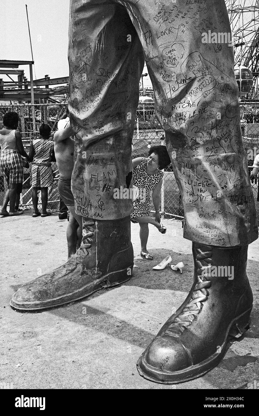 Eine Frau Änderungen ihre Schuhe, lehnte sich gegen die Beine eines riesigen Statue mit Signaturen. Stockfoto