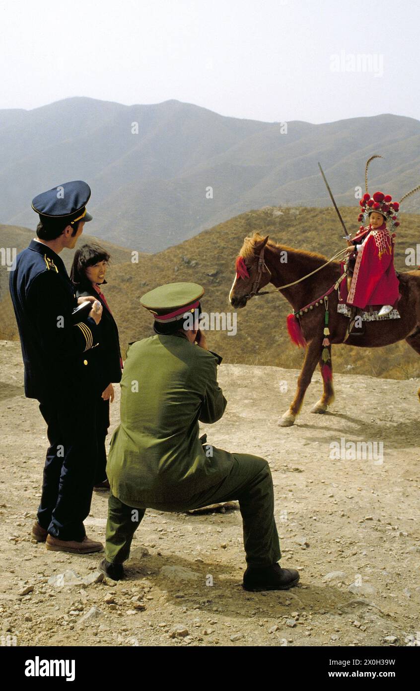 Chinesische Touristen fotografieren sie einen kostümierten Kind mit Schwert auf einem Pferd in duftenden Hügeln Park. Stockfoto