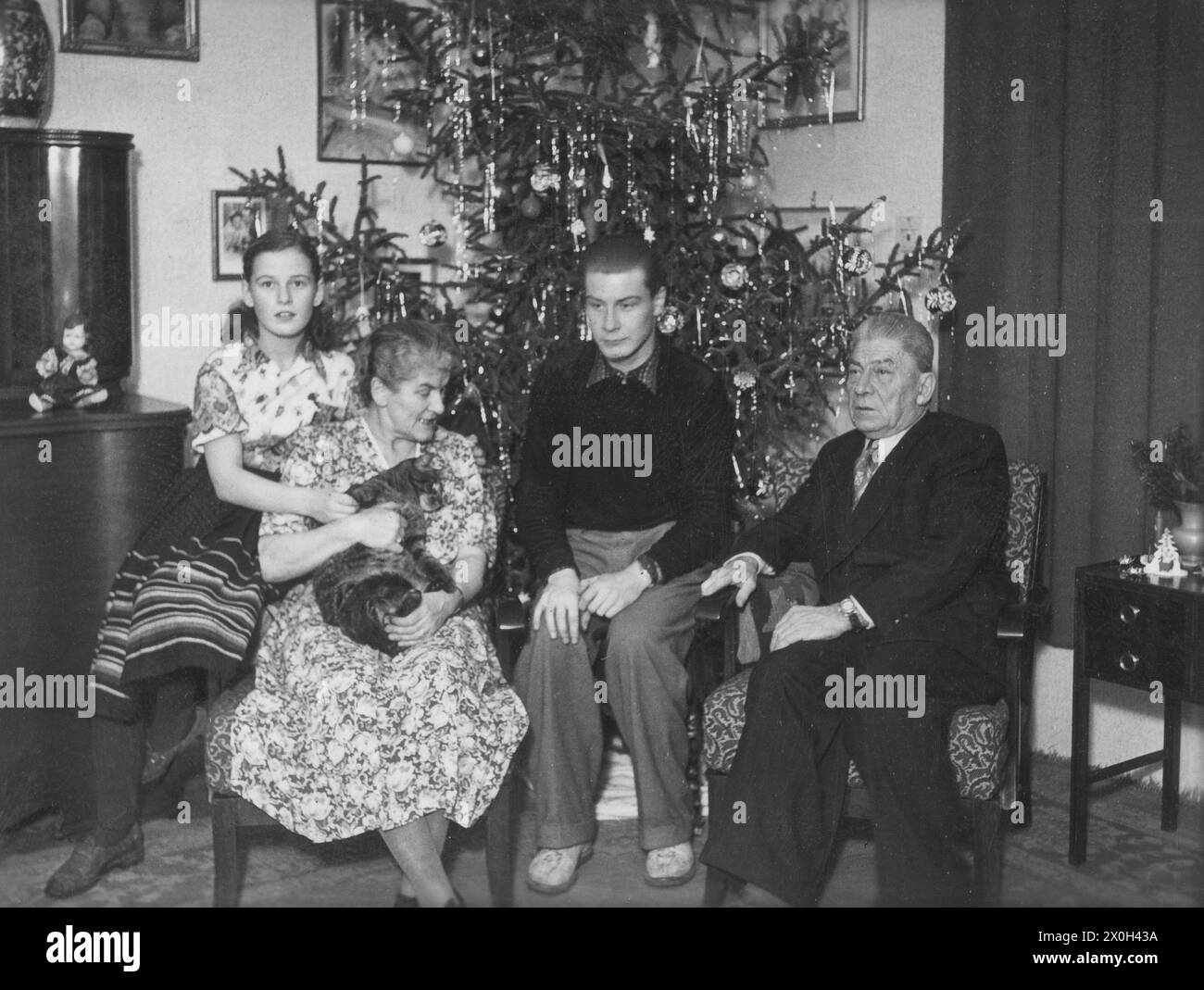 Vor dem dekorierten Weihnachtsbaum sitzt eine Familie. [Automatisierte Übersetzung] Stockfoto