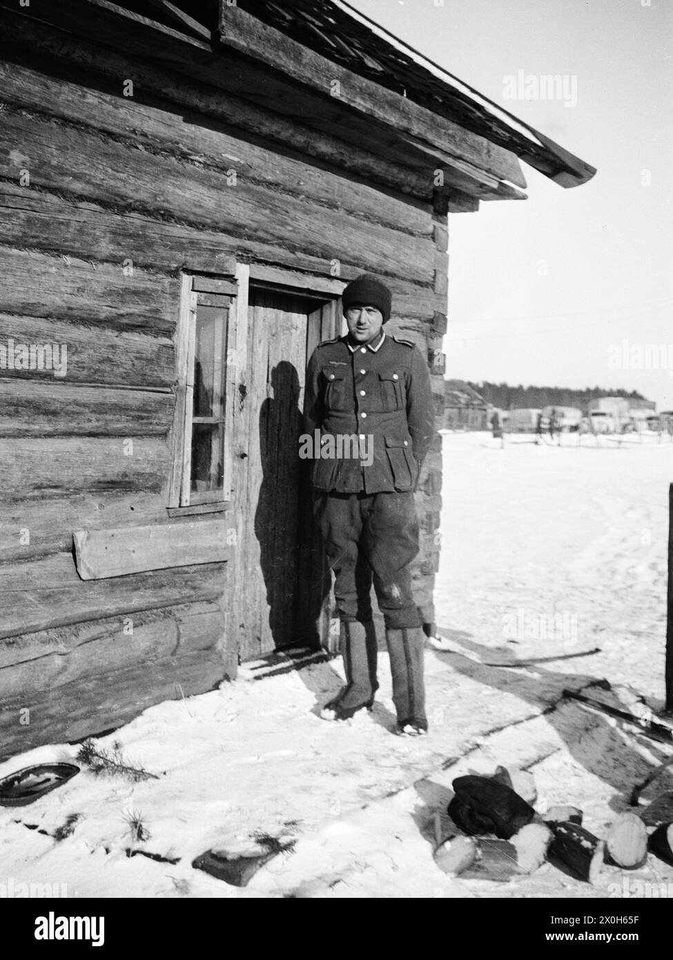 Mit Filzgamaschen und einem Wackelhut steht ein Unteroffizier vor einer Hütte. Das Bild wurde von einem Mitglied des Radfahrgrenadierregiments 2/Radfahrsicherungsregiment 2 im Nordteil der Ostfront aufgenommen. [Automatisierte Übersetzung] Stockfoto