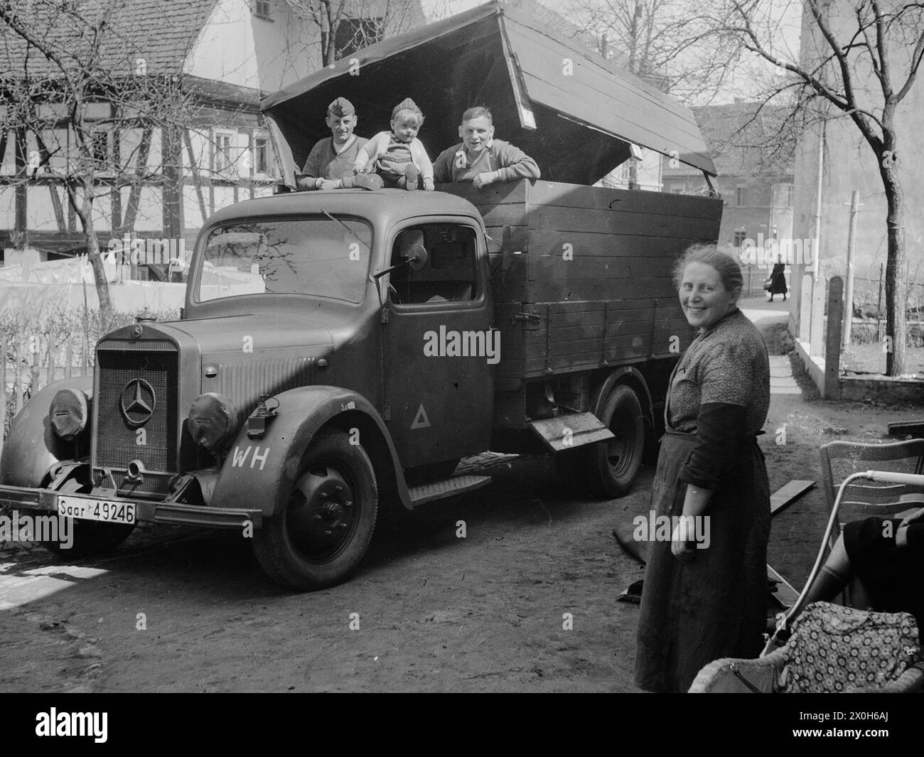 Zwei Wehrmachtssoldaten arbeiten auf dem Rücksitz eines Lastwagens. Ein kleiner Junge sitzt auf dem Dach des Fahrerhauses. [Automatisierte Übersetzung] Stockfoto