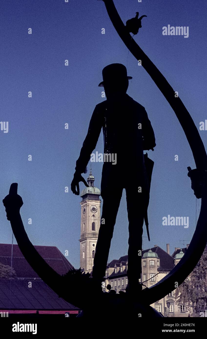Silhouette des Karl-Valentin-Brunnens am Viktualienmarkt in München mit der Heilig-Geist-Kirche im Hintergrund. [Automatisierte Übersetzung] Stockfoto