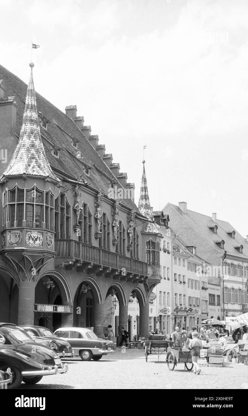 Seitenansicht des historischen Kaufhauses mit seinen Erkerfenstern. Vor ihm stehen die Marktstände auf dem Münsterplatz voller Aktivität. [Automatisierte Übersetzung] Stockfoto