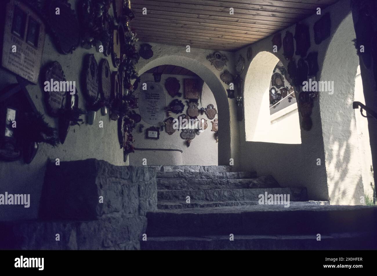 Treppe zur katholischen Wallfahrt- und Votivkirche im Stadtteil Partenkirchen. Votivtafeln hängen an den Wänden. [Automatisierte Übersetzung] Stockfoto