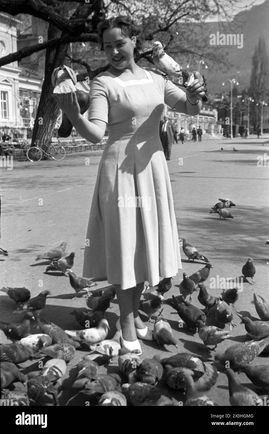 Eine junge Frau in einem hellen Kleid, das Tauben in einem Park füttert. [Automatisierte Übersetzung] Stockfoto