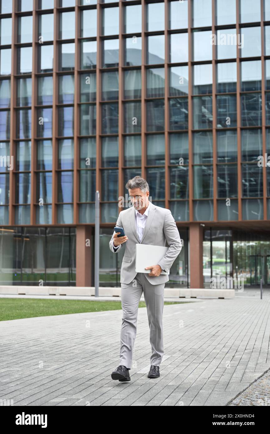 Geschäftiger Geschäftsmann mittleren Alters, der das Telefon benutzt, läuft auf der Straße der Stadt, voller Körper. Stockfoto