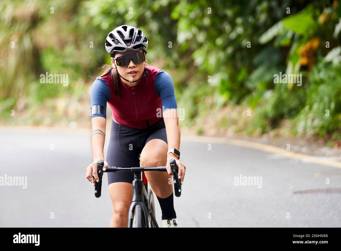 Junge asiatische Frau Radfahrerin, die draußen auf der Landstraße Fahrrad fährt Stockfoto
