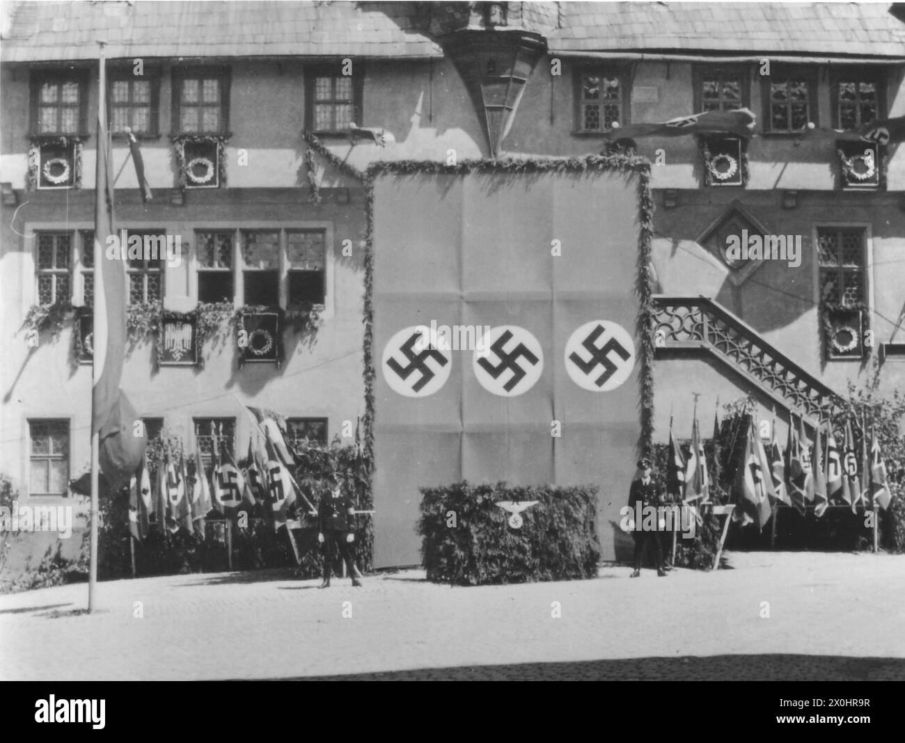 Zwei SS-Dienstposten stehen vor dem Dreibund für die Rede von Funktionären der NSDAP mit dem Adler vor dem Rathaus in Ochsenfurt anlässlich der Feierlichkeiten zum Arbeitstag am 1. Mai 1933. [Automatisierte Übersetzung] Stockfoto