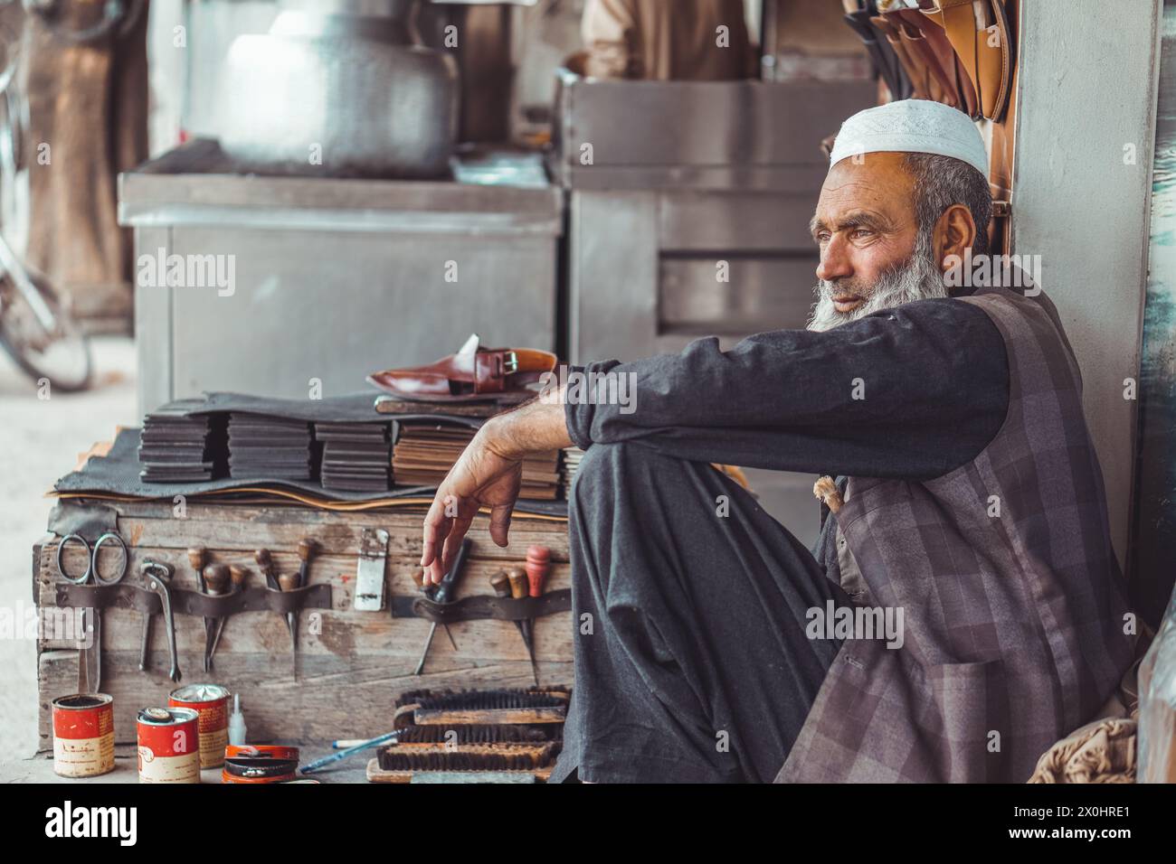 Der arme alte pakistanische Pathan Schuhmacher ist auf den Straßen Pakistans mit seinen handgefertigten Lederschuhen und Reparaturwerkzeugen in seinem Straßenladen Stockfoto