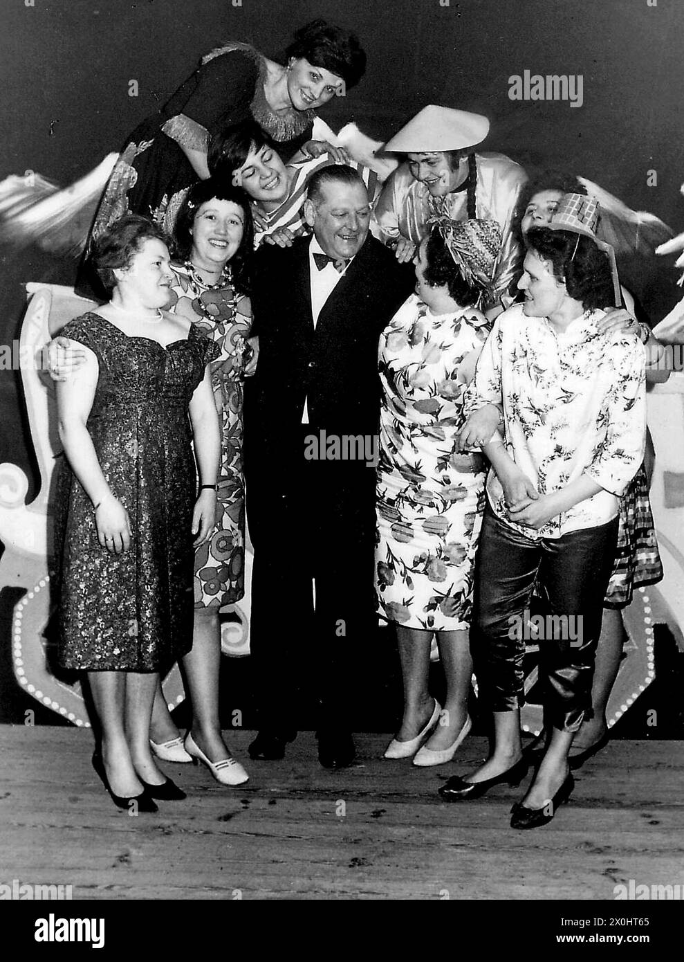 Ein älterer Mann in einem Anzug, der bei einer Karnevalsfeier in Ochsenfurt von verkleideten Frauen umgeben ist. [Automatisierte Übersetzung] Stockfoto