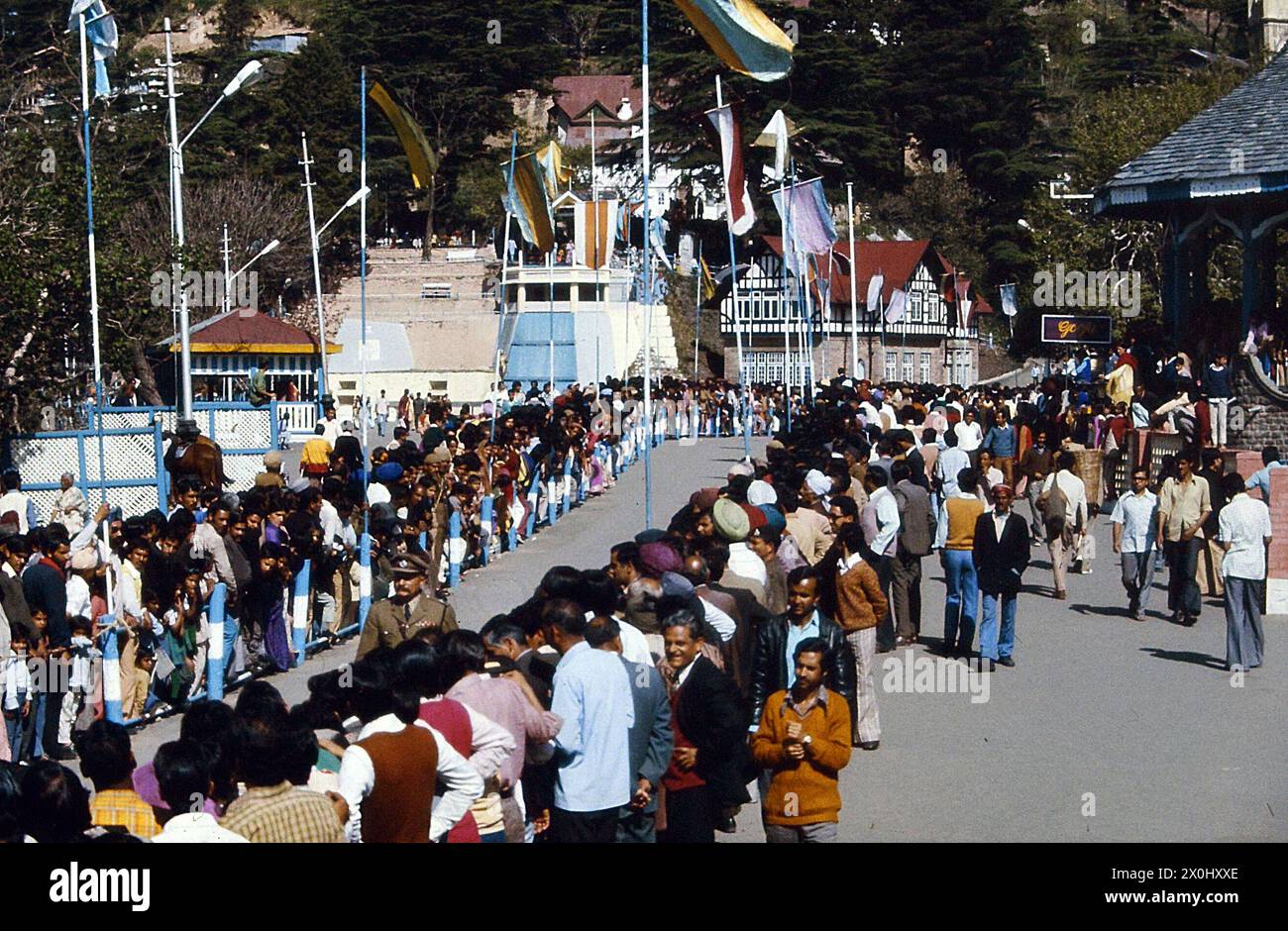 Die Zuschauer warten auf den Besuch der ehemaligen indischen Premierministerin Indira Gandhi in Shimla. Sie führen eine eng gepackte Straße. Es ist mit Flaggen dekoriert. Auf der Straße läuft ein uniformierter Mann den Gang hinunter. [Automatisierte Übersetzung] Stockfoto