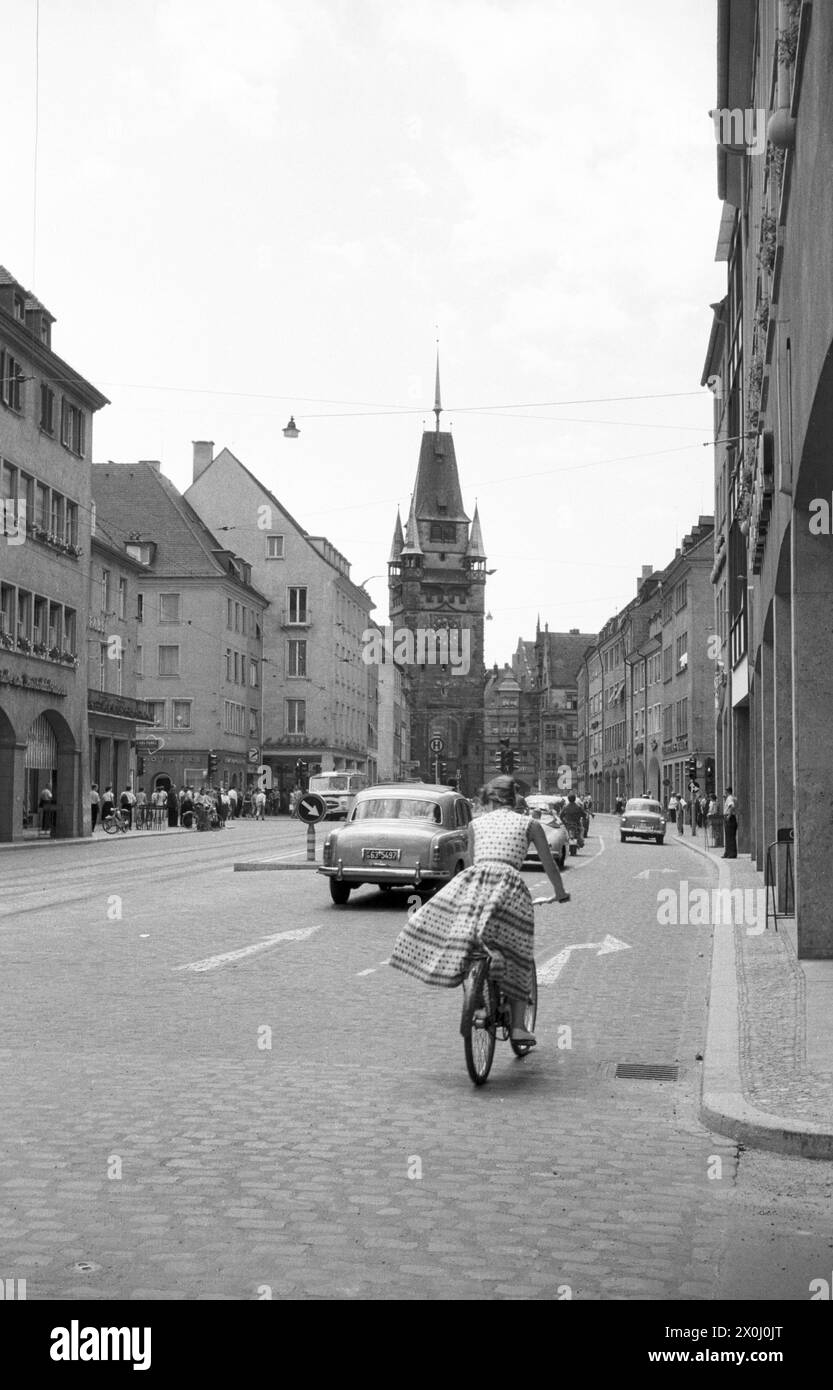 Eine Frau fährt mit dem Fahrrad auf der Kaiser-Joseph-Straße, die mit Autos beschäftigt ist. Der Martinstor im Hintergrund. [Automatisierte Übersetzung] Stockfoto