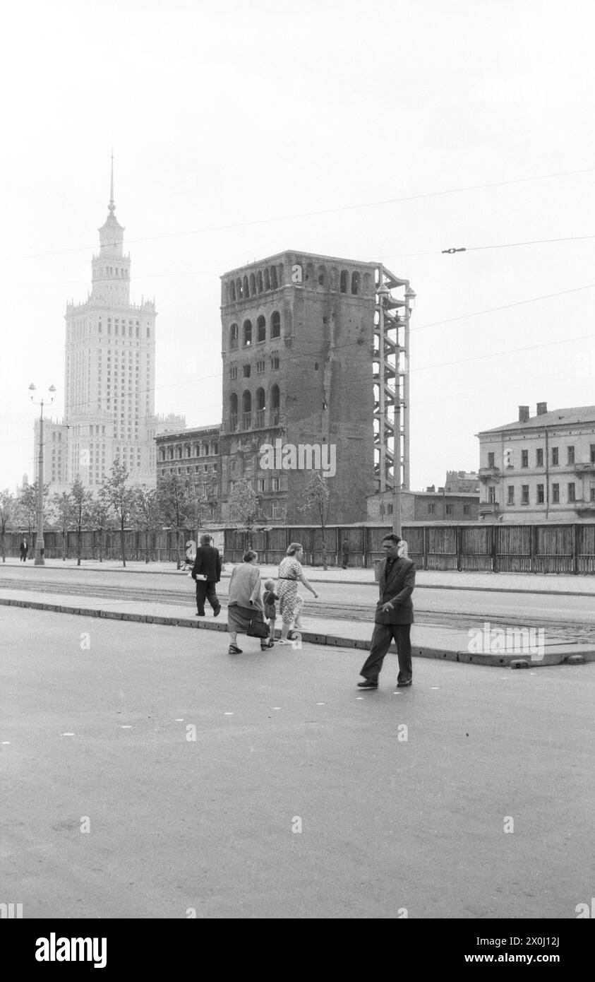 Einige Passanten überqueren eine breite Straße, auf der es keine Autos gibt. Hinter einem langen Bauzaun, einer Ruine. Im Hintergrund befindet sich der Palast für Kultur und Wissenschaft. [Automatisierte Übersetzung] Stockfoto