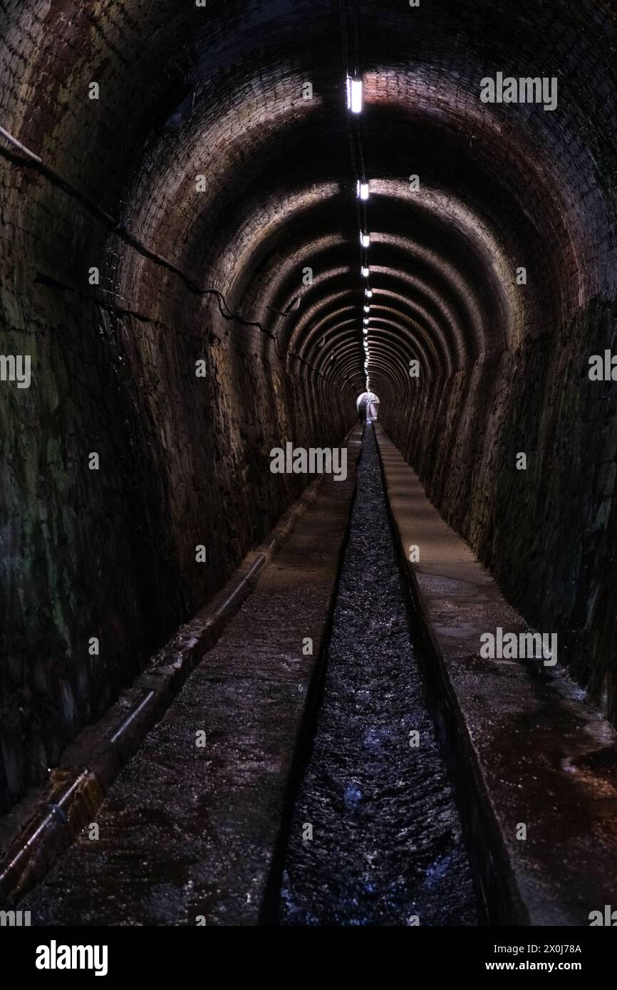Langer Tunnel, beleuchtet von künstlichen Lichtern, umgeben von Wänden auf beiden Seiten, Wasserkanal Stockfoto