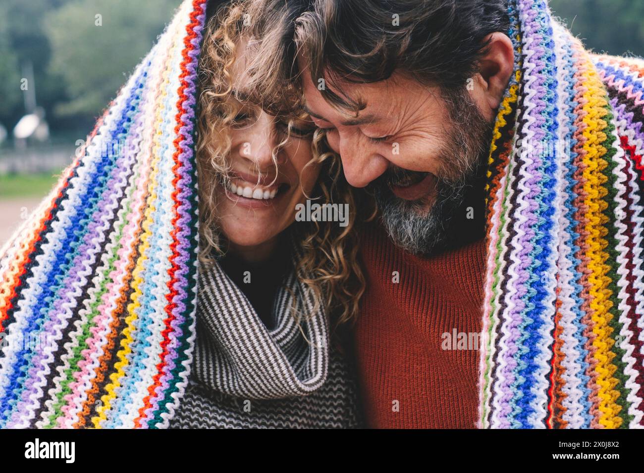 Überglücklich erwachsenes kaukasisches Paar unter einem bunten Cover lacht und hat Spaß zusammen mit Liebe und Freundschaft. Junge ältere Menschen in Outdoor-Freizeit romantische Aktivität. Mann und Frau lachen viel Stockfoto