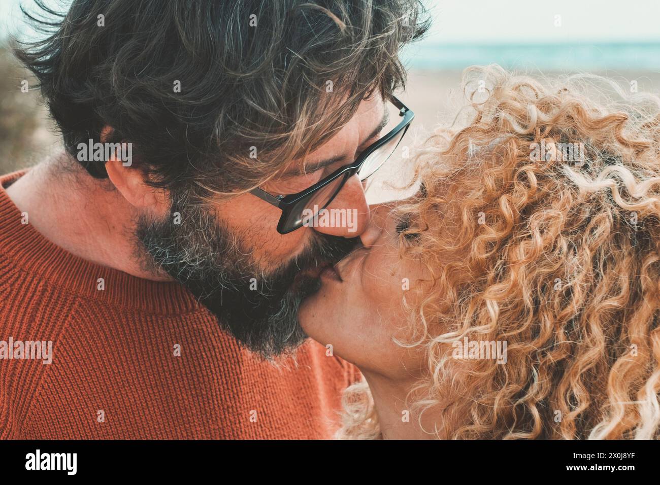 Erwachsene Menschen Mann und Frau in Liebe und Beziehung küssen am Strand mit Meer im Hintergrund. Ein Paar in einer glücklichen Beziehung hat romantische Freizeit zusammen mit Zärtlichkeit und Kuss Stockfoto