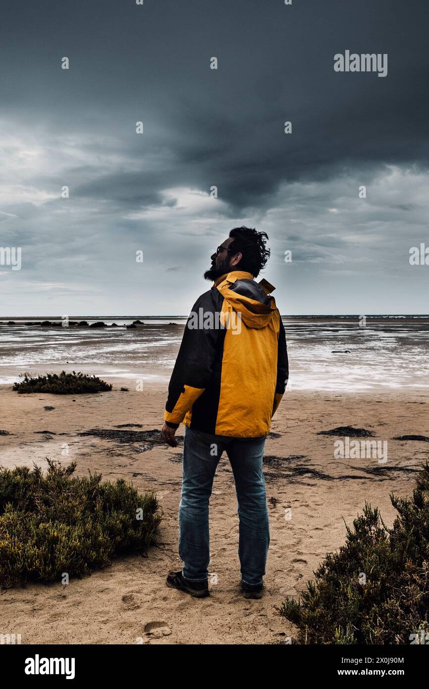 Epischer Standmann gegen schlechtes Wetter und schwarze Wolken im Hintergrund am Strand. Winter Saison Abenteuer Freizeit Aktivität Menschen Konzept. Stockfoto