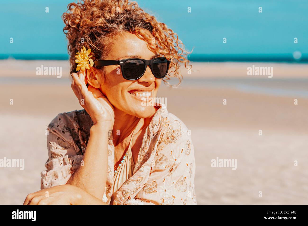 Porträt eines glücklichen Touristen, der am Strand sitzt und lächelt, mit blauem Himmel und Meer im Hintergrund. Reisen und Tourismus im Sommerurlaub. Weibliche Menschen mit Sonnenbrillen auf dem Sand Stockfoto Porträt eines glücklichen Touristen, der am Strand sitzt und lächelt, mit blauem Himmel und Meer im Hintergrund. Reisen und Tourismus im Sommerurlaub. Weibliche Menschen mit Sonnenbrillen auf dem Sand Stockfoto