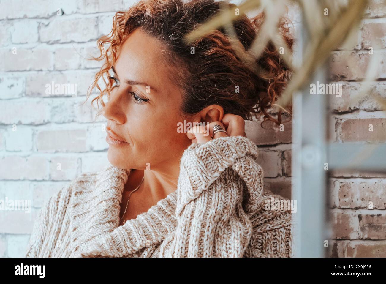 Seitliches Porträt einer erwachsenen attraktiven Dame mit ernstem und treuem Ausdruck zu Hause vor einer Ziegelmauer. Weibliche Menschen und persönliche Probleme. Traurigkeit und schlechtes Lifestyle-Konzept Stockfoto