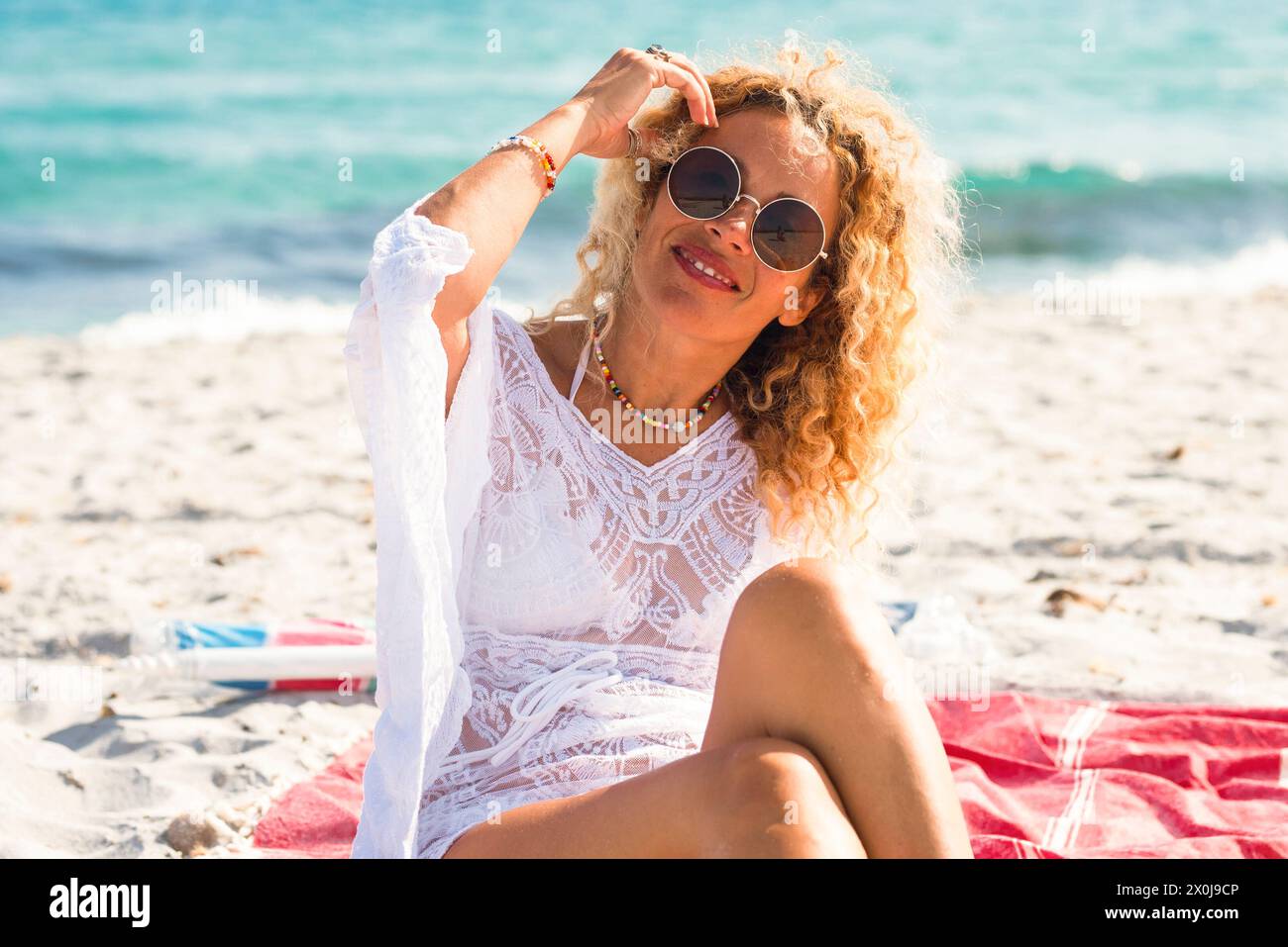 Porträt einer Frau mit einem Lächeln und einem Posen am Strand auf weißem Sand und blauem Ozean im Hintergrund. Happy Tourism Freizeitangebot Konzept. Weibliche Menschen im Sommerferienleben Stockfoto