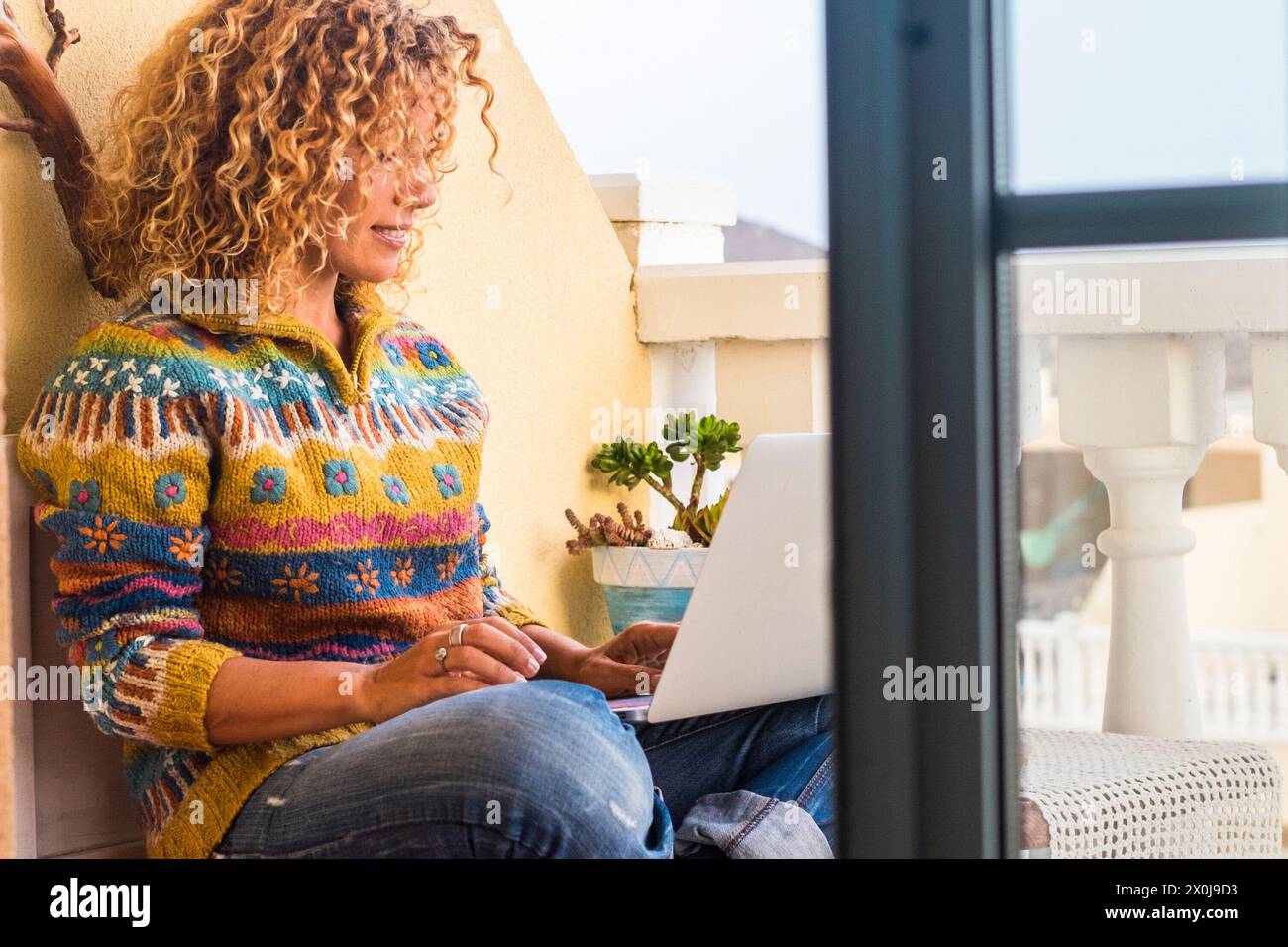 Frau, die zu Hause draußen sitzt und am Laptop arbeitet. Konzept des intelligenten Arbeitens und von Menschen mit Online-Jobs. Glückliche Erwachsene, weibliche Lächeln und nutzen Sie die Technologie mit drahtloser Internetverbindung Stockfoto