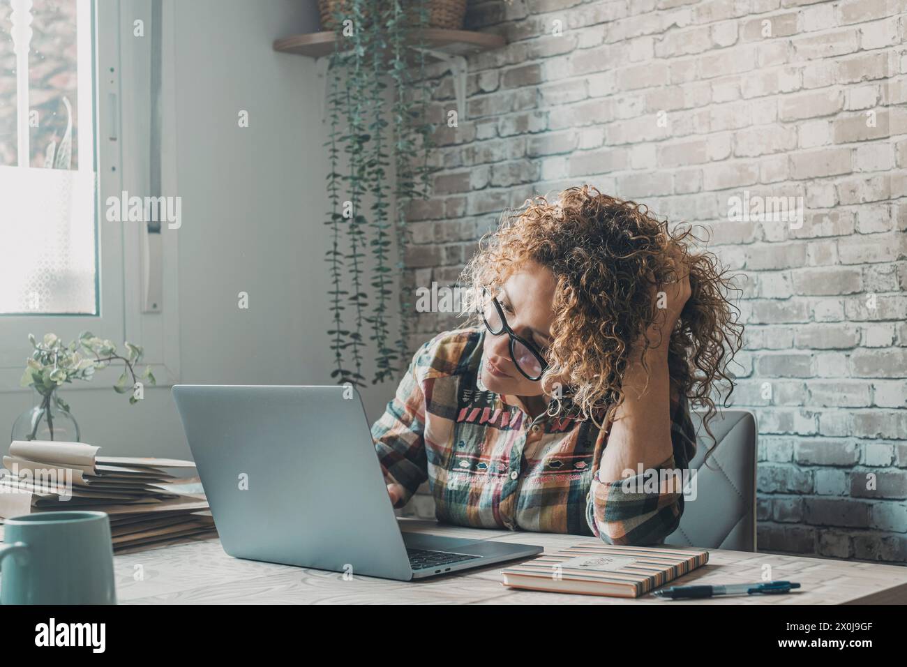 Eine moderne freischaffende Unternehmerin, die zu Hause an einem Laptop arbeitet, in einem kleinen Büro, berührt ihren Kopf und schaut mit Zweifeln und Neugier auf den Display-Computer. Online-Frauen Stockfoto