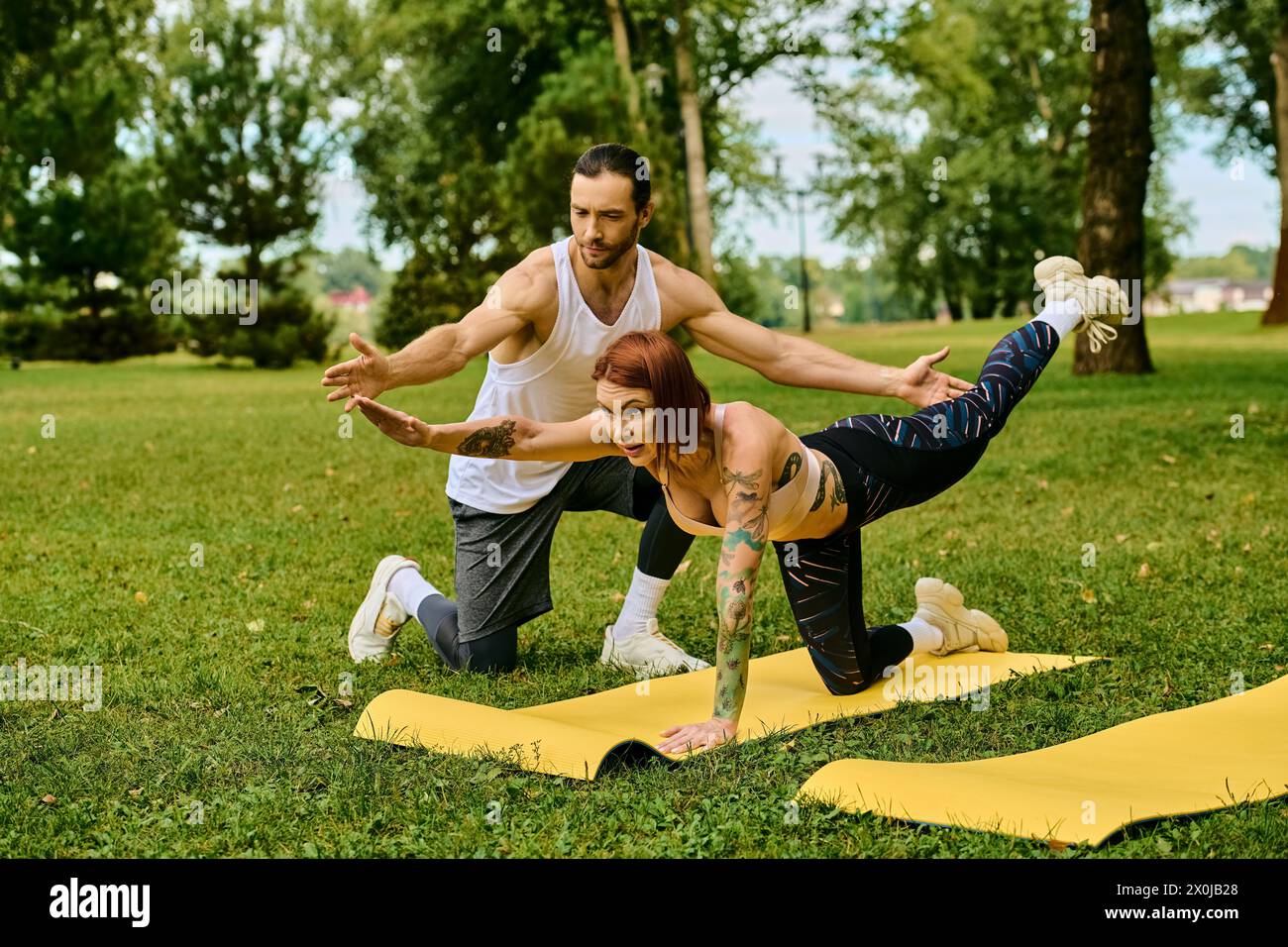 Eine Frau in Sportbekleidung übt Yoga im Freien mit Entschlossenheit und Motivation, geführt von einem Personal Trainer. Stockfoto
