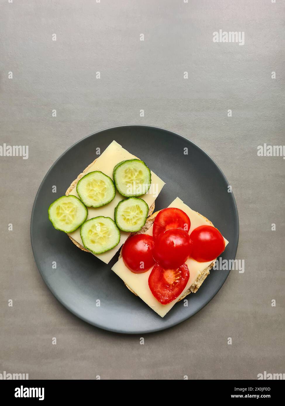 Zwei Brotscheiben mit Käse, Gurke und Tomate, in Scheiben geschnitten Stockfoto