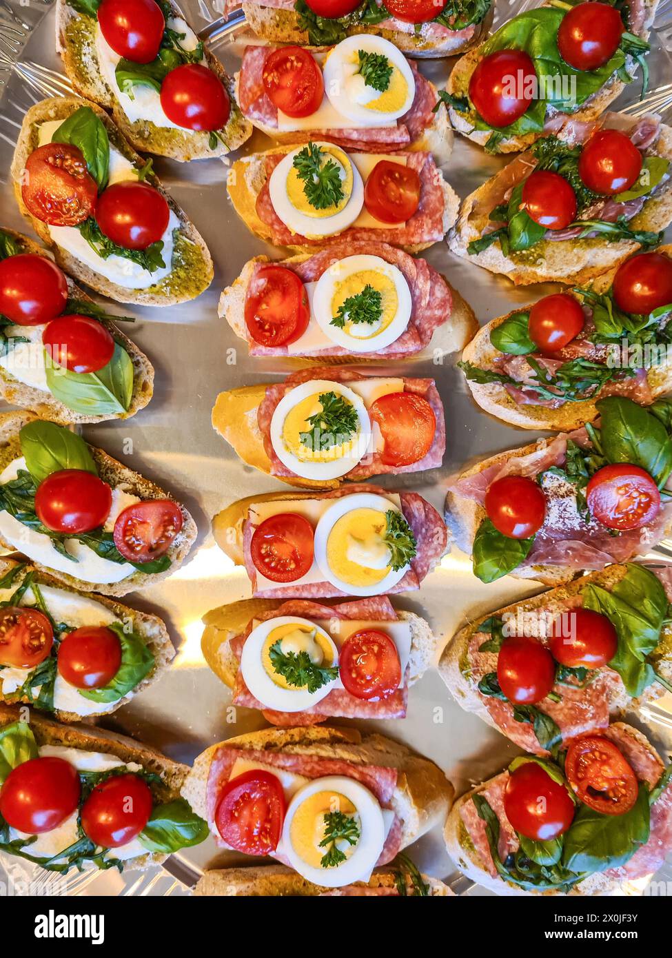 Brotscheiben mit Salami, in Scheiben geschnittenen Eiern, Tomaten, Mozzarella, Petersilie, basilikum-Blätter, grüner Pesto-Aufstrich Stockfoto