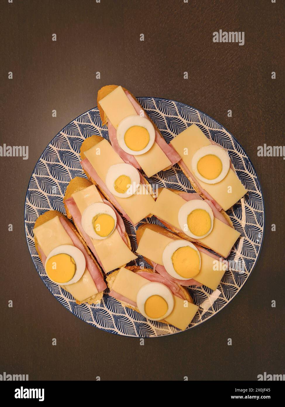Hartgekochte Eier in Scheiben mit Käse und Schinken, serviert auf Brotscheiben auf einem Teller Stockfoto