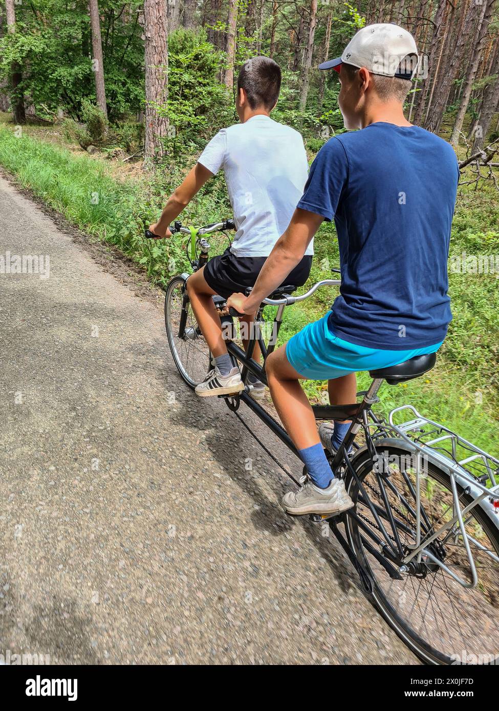 Zwei Teenager, die auf einer schmalen Straße durch einen grünen Wald im Ferienort Prerow, Fischland Darß, Mecklenburg-Vorpommern fahren Stockfoto