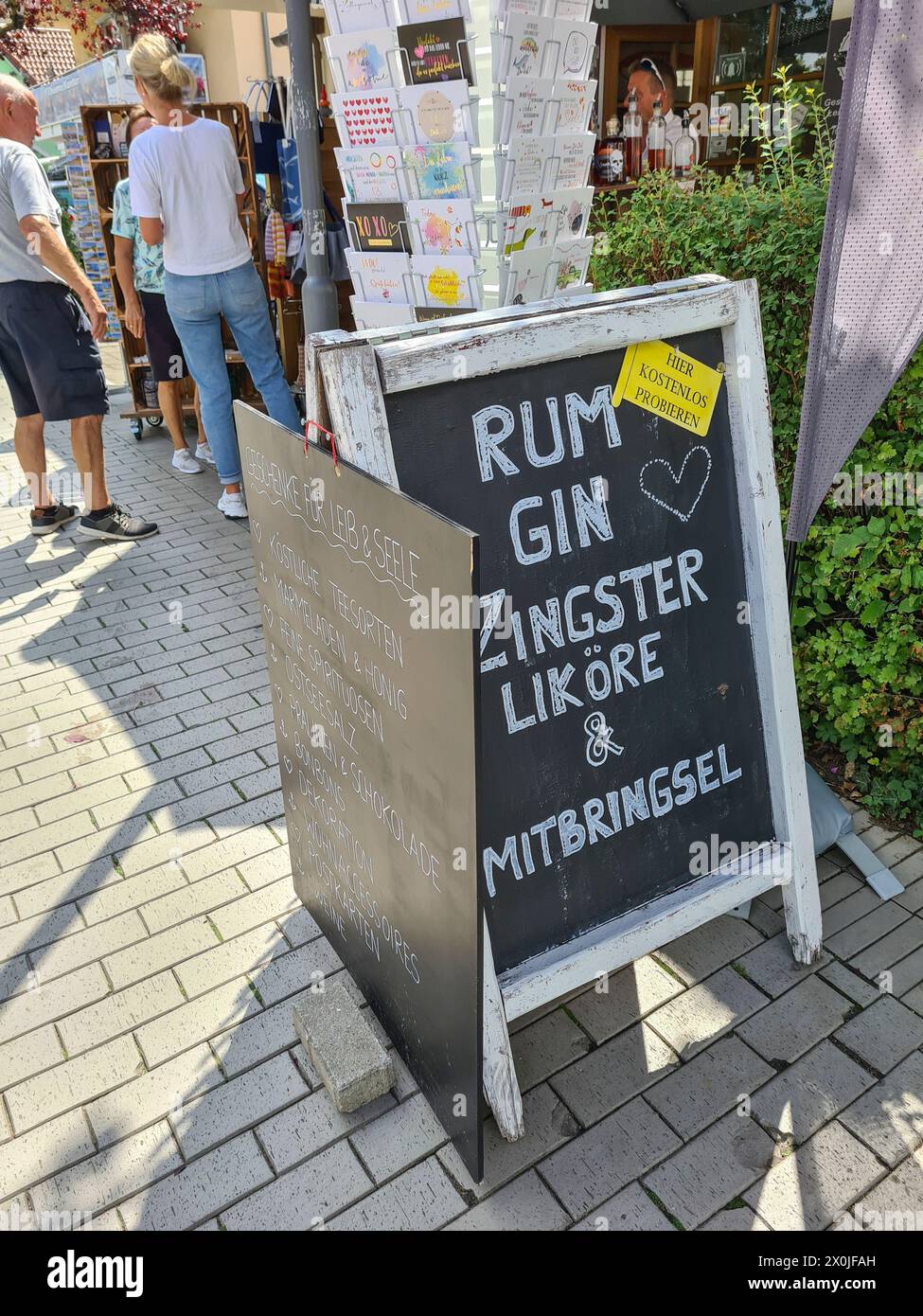 Ein handgeschriebenes Werbeschild steht vor dem Geschäft, das Rum, Gin, Souvenirs und Liköre von Zingst, Touristen im Hintergrund, Ostseebad Zingst, Deutschland, anbietet Stockfoto