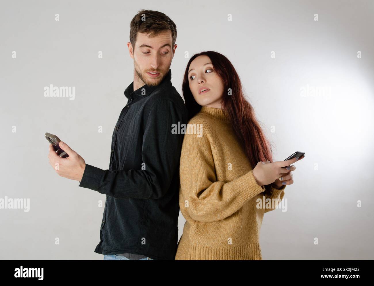 Eifersüchtiges Paar, das sich gegenseitig auf das Handy sieht. Beide spionieren und kontrollieren einander. Stockfoto
