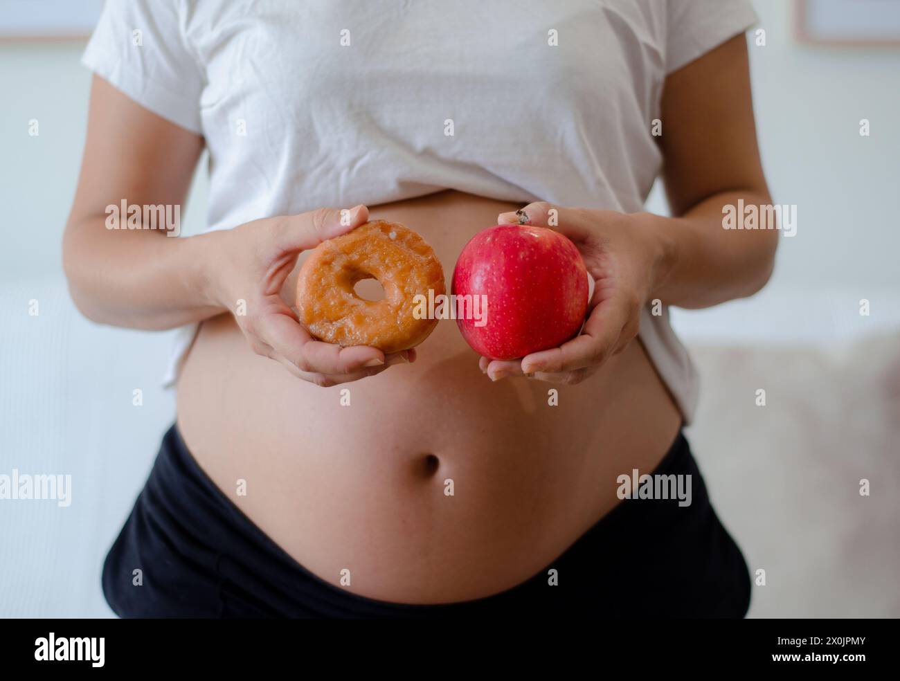 Schwangere Frau, die zögert, einen Donut oder einen Apfel zu essen. Pränatale Ernährung und gesundes Gewohnheitskonzept. Stockfoto