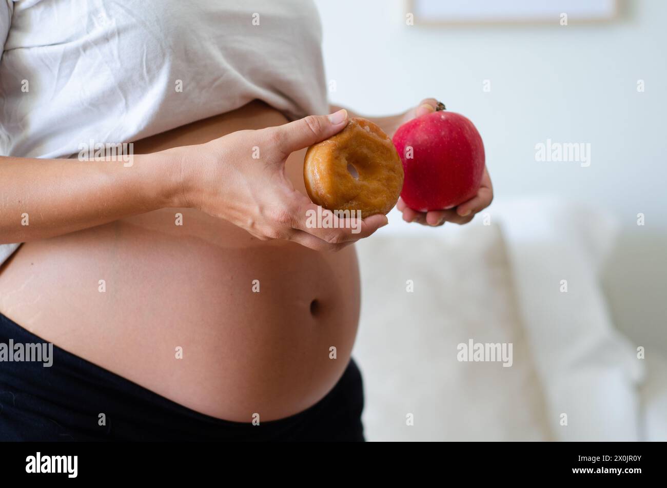 Schwangere Frau, die zögert, einen Donut oder einen Apfel zu essen. Pränatale Ernährung und gesundes Gewohnheitskonzept. Stockfoto