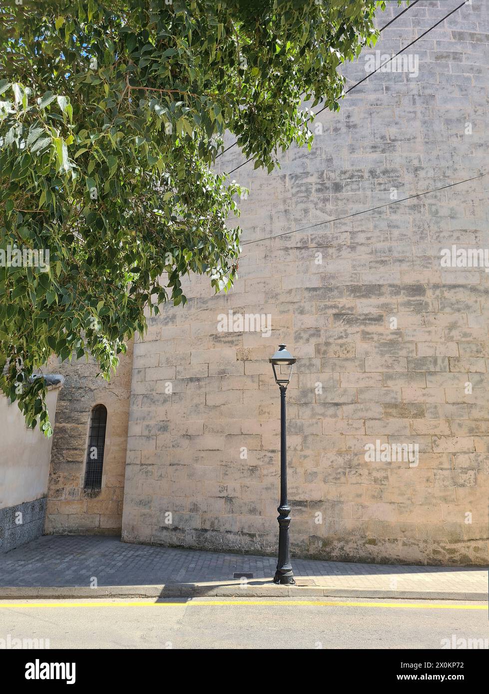 Blick auf eine alte antike Straßenlaterne in Porto Christo, ein grüner Baum an der Seite, Straßenszene im Sommer mit Sonne und Schatten, Mallorca, Spanien Stockfoto