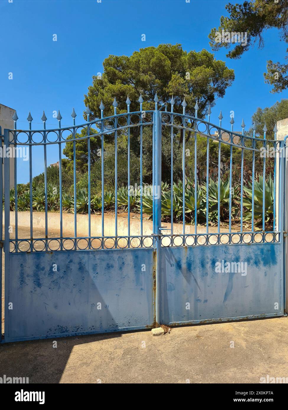 Blick von der Straße auf ein blaues Tor in der Einfahrt zu einem privaten Grundstück im Sonnenlicht, Mallorca, Spanien Stockfoto