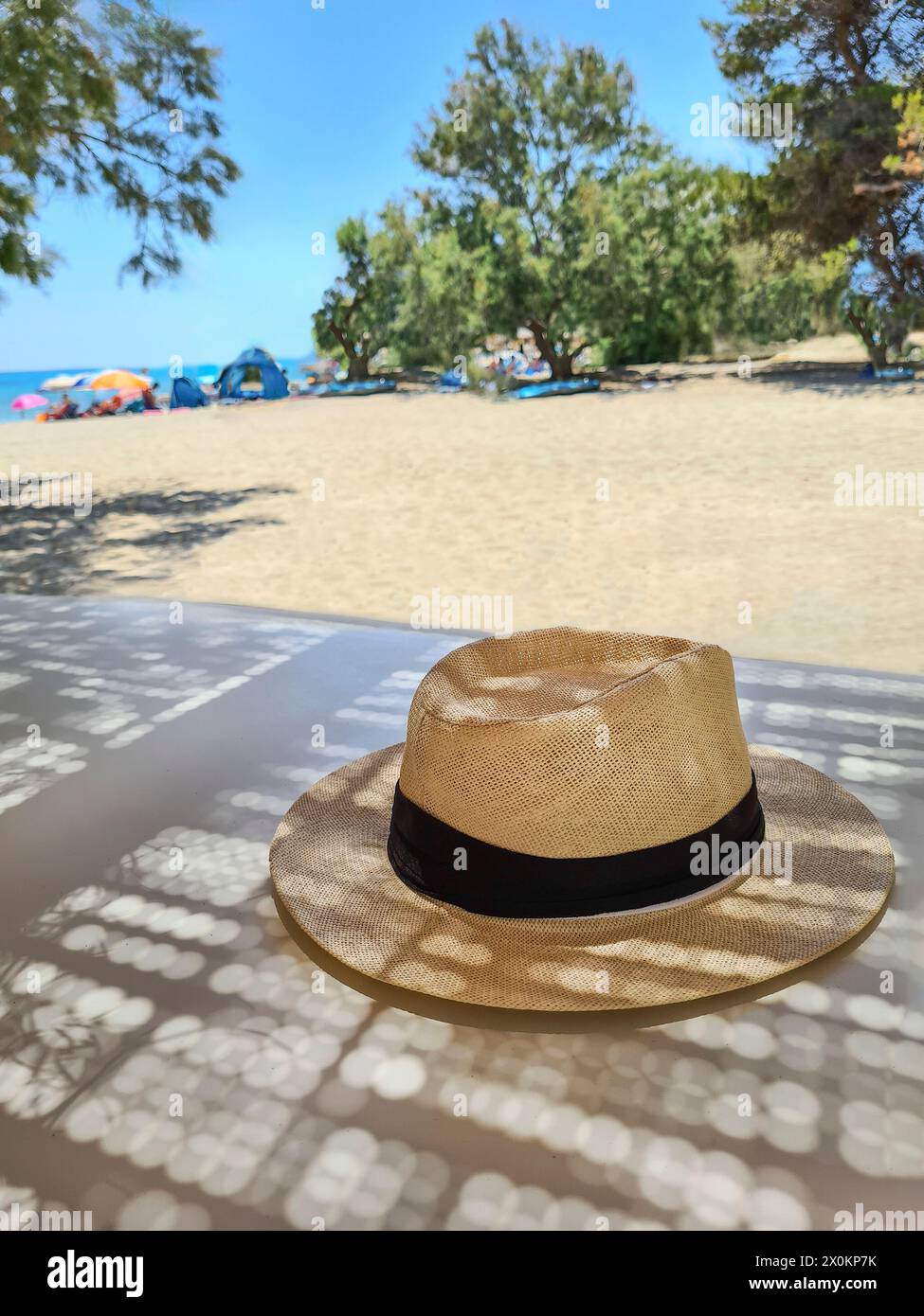 Ein Strohhut liegt im Schatten auf einem Tisch in den Sommerferien, verschwommener Hintergrund, Schwerpunkt liegt auf Strohhut als Sonnenschutz, Mallorca, Spanien Stockfoto