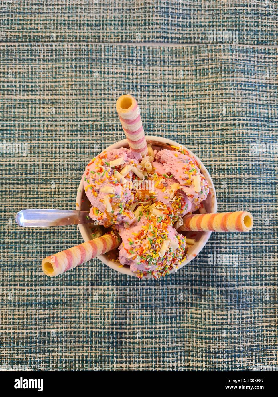 Ein farbenfroher Eisbecher mit drei Schaufeln Erdbeereis und bunten Streuseln, garniert mit drei gestreiften Eiskegeln, Mallorca, Spanien Stockfoto